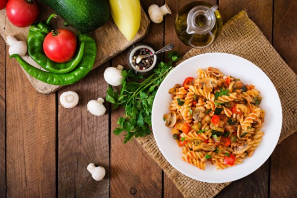 vegetarian-vegetable-pasta-fusilli-with-zucchini-mushrooms-and-capers-in-white-bowl-on-wooden-table_2829-432
